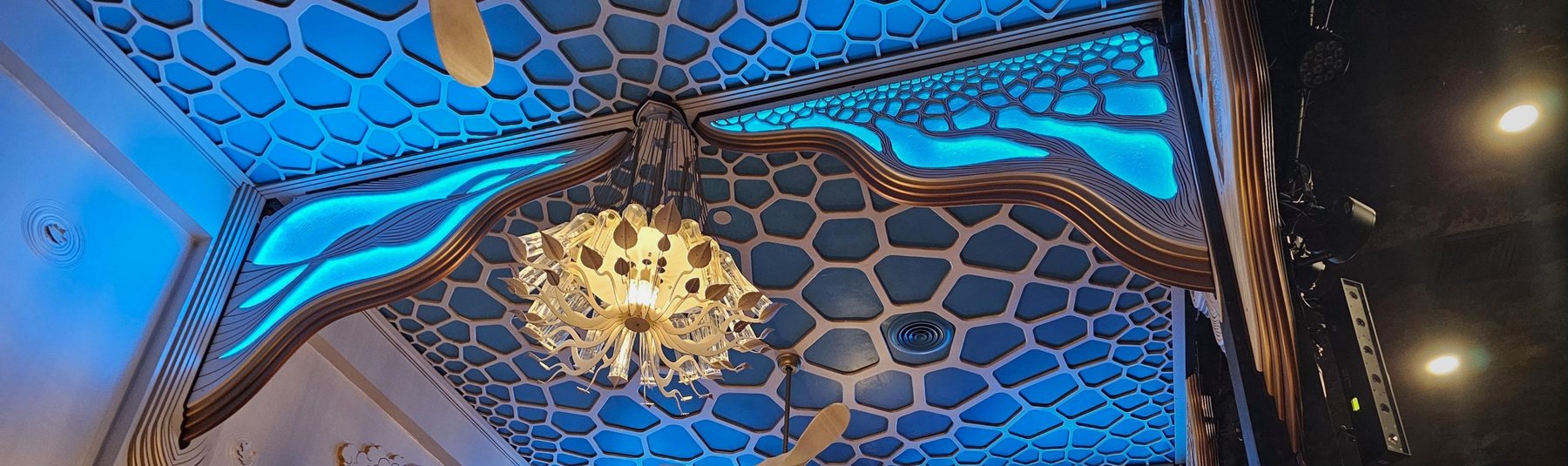 Glowing blue organic ceiling panels and carved wooden arches around a glass chandelier